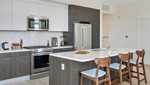 A modern kitchen with a central island, stainless steel appliances, and wooden bar stools.