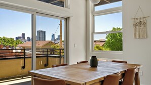 A dining area with a wooden table and leather chairs, large windows with a city view, and a macrame wall hanging.