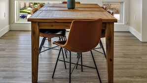 A dining area with a wooden table and chairs, large windows, and a hanging light fixture.