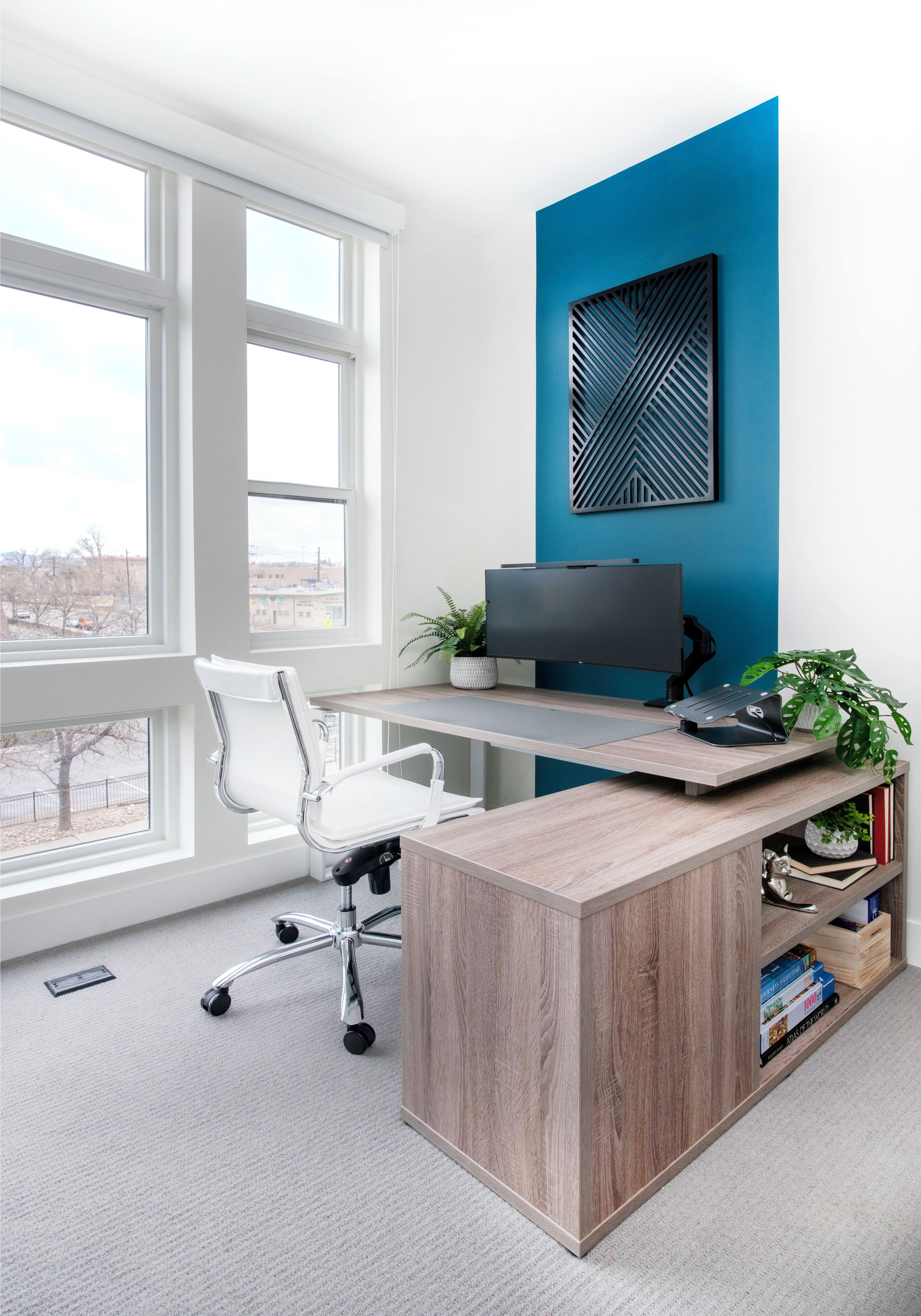 A modern office with a large window, a desk with a computer, a white chair, and a blue accent wall.