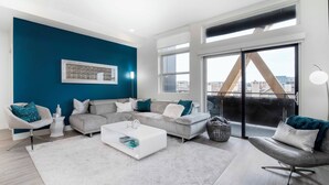 Een moderne woonkamer met een grijze modulaire bank, een witte salontafel en uitzicht op de stad door grote ramen.