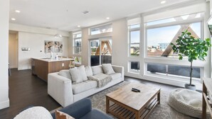 A modern living room with a sofa, coffee table, and a view of the city through large windows. - Rose All Day | 2BR LoHi Loft | Walk to Ball Arena | Dog-Friendly (Denver)