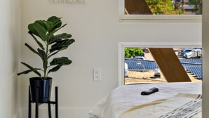 Une chambre avec un lit, une plante en pot, une décoration murale en macramé et une vue sur des panneaux solaires à l’extérieur.