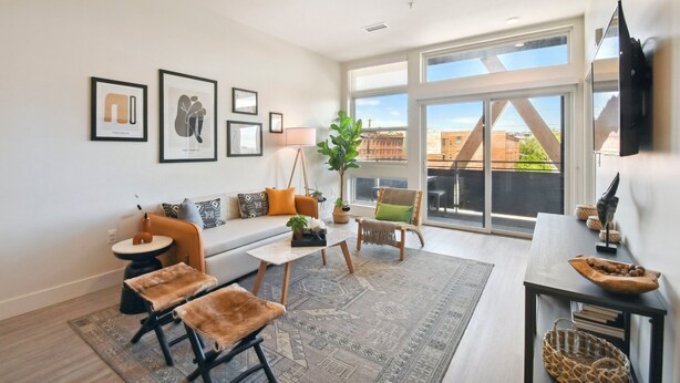 Una sala de estar moderna con sofá, mesa de centro y sillones, ventanas amplias con vista a la ciudad y obras de arte en las paredes.