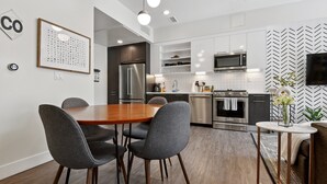 Una cocina moderna con zona de comedor, que presenta una mesa de madera, sillas grises y electrodomésticos integrados.