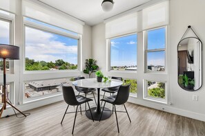 A modern dining area with a round table, black chairs, and large windows offering city views.