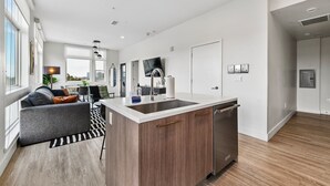 Et moderne køkken med en central ø, rustfrie apparater og et spiseområde med sofa og bord.