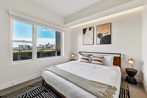 A modern bedroom with a large bed, two bedside tables, and a city view.