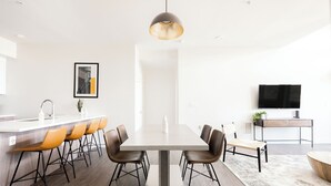 Una cocina moderna con una isla central, taburetes de bar, una lámpara colgante y un televisor de pantalla plana sobre un soporte.
