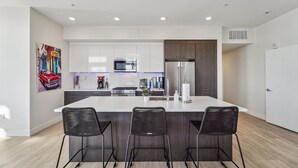 A modern kitchen with white cabinets, a stainless steel refrigerator, and a central island with bar stools.