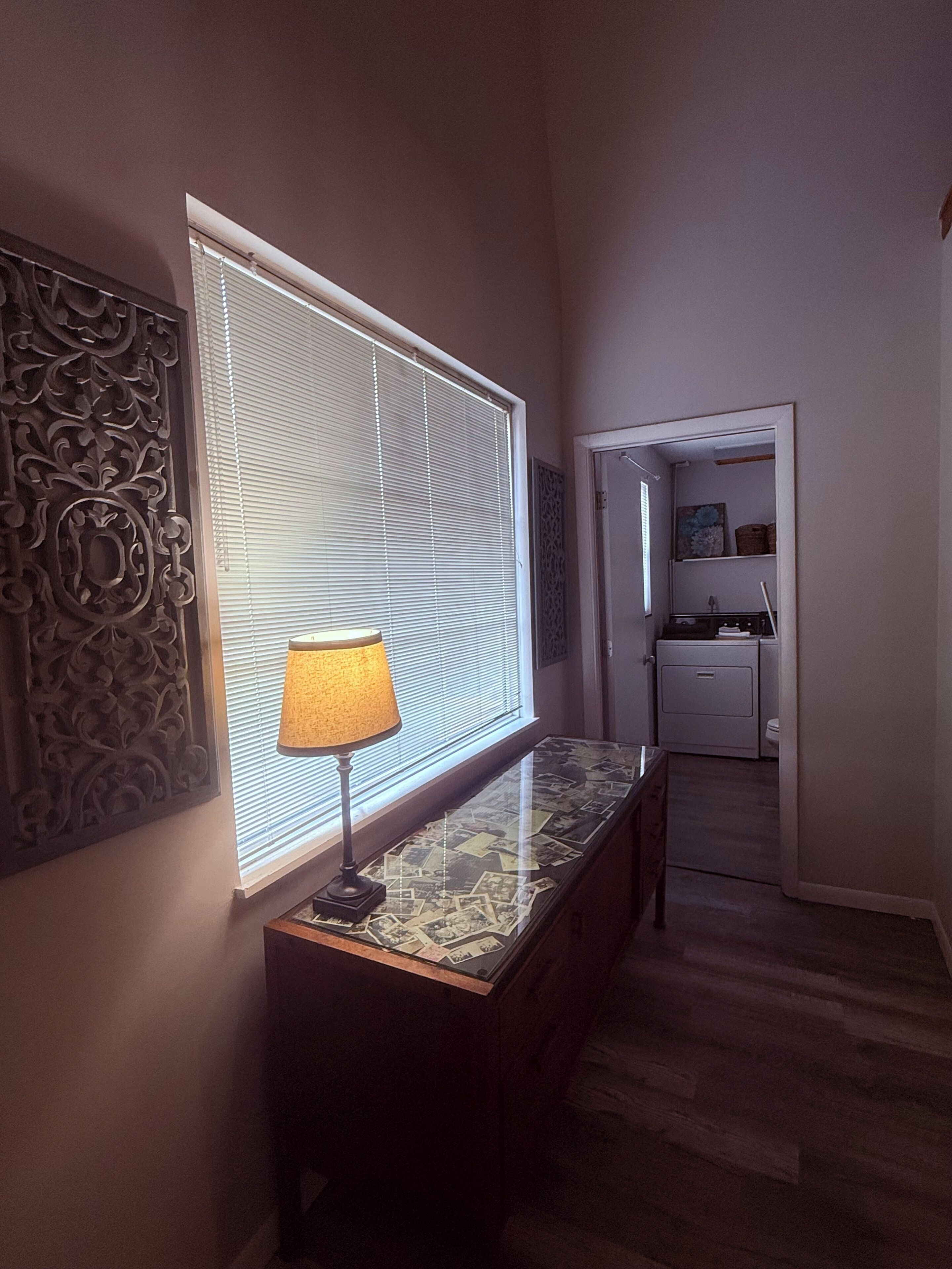 Un pasillo con una lámpara sobre una consola, un panel decorativo en la pared y una puerta que da a una cocina.