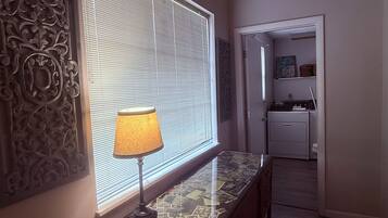 Un pasillo con una lámpara sobre una consola, un panel decorativo en la pared y una puerta que da a una cocina.
