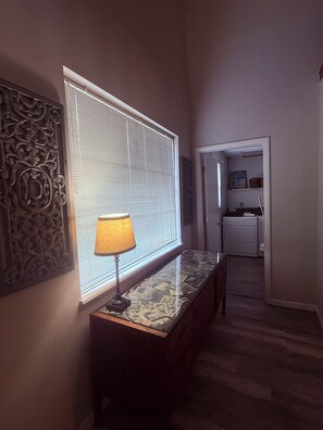 A hallway with a lamp on a console table, a decorative wall panel, and a door leading to a kitchen area.