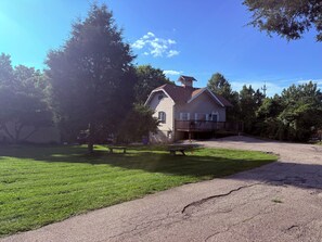 A two-story house with a front deck, surrounded by a well-maintained lawn and trees. - Cozy Cottage on New London (Hamilton)
