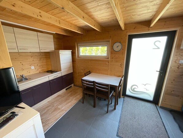 A compact kitchen with wooden cabinets, a dining table with chairs, a clock on the wall, and a window. - LILLY 5 STARS - 140m to the beach - the sound of the sea on the terrace guaranteed! (Grzybowo)