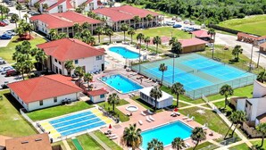 Une vue aérienne d’un complexe hôtelier doté de plusieurs piscines, de courts de tennis et de différents bâtiments aux toits rouges.