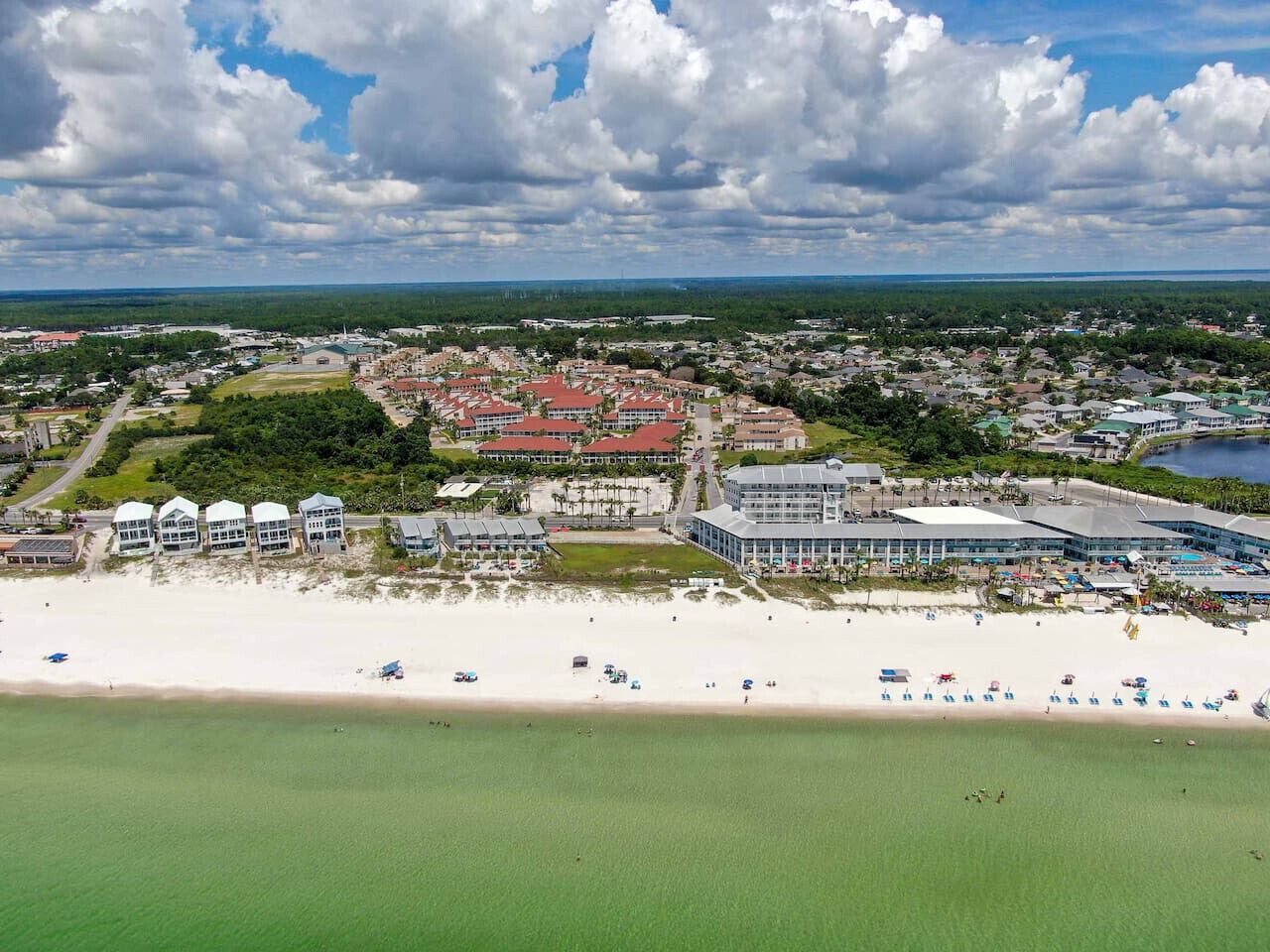 Vista aerea di una località costiera con spiaggia, diversi edifici e un grande complesso alberghiero.