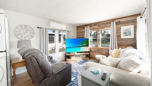 Una sala de estar moderna con un televisor de pantalla plana grande, un sofá gris, un sofá beige y una pequeña mesa con un control remoto.