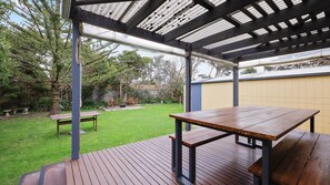 An outdoor patio with wooden tables and benches, a pergola structure, and a grassy backyard.