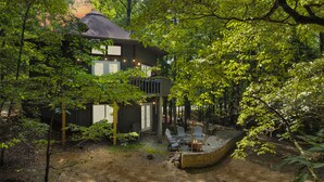 A two-story house with a balcony, surrounded by dense trees. - Large Octagon Cabin on Double Lot! Hot Tub, Fire place, Game room, Fire pit! (Ellijay)