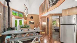A wooden interior with a stone wall, a wooden dining table, benches, a refrigerator, and a staircase. - Large Octagon Cabin on Double Lot! Hot Tub, Fire place, Game room, Fire pit! (Ellijay)