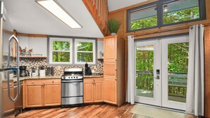 A modern kitchen with wooden cabinets, a stainless steel stove, and large windows offering a view of the outdoors. - Large Octagon Cabin on Double Lot! Hot Tub, Fire place, Game room, Fire pit! (Ellijay)