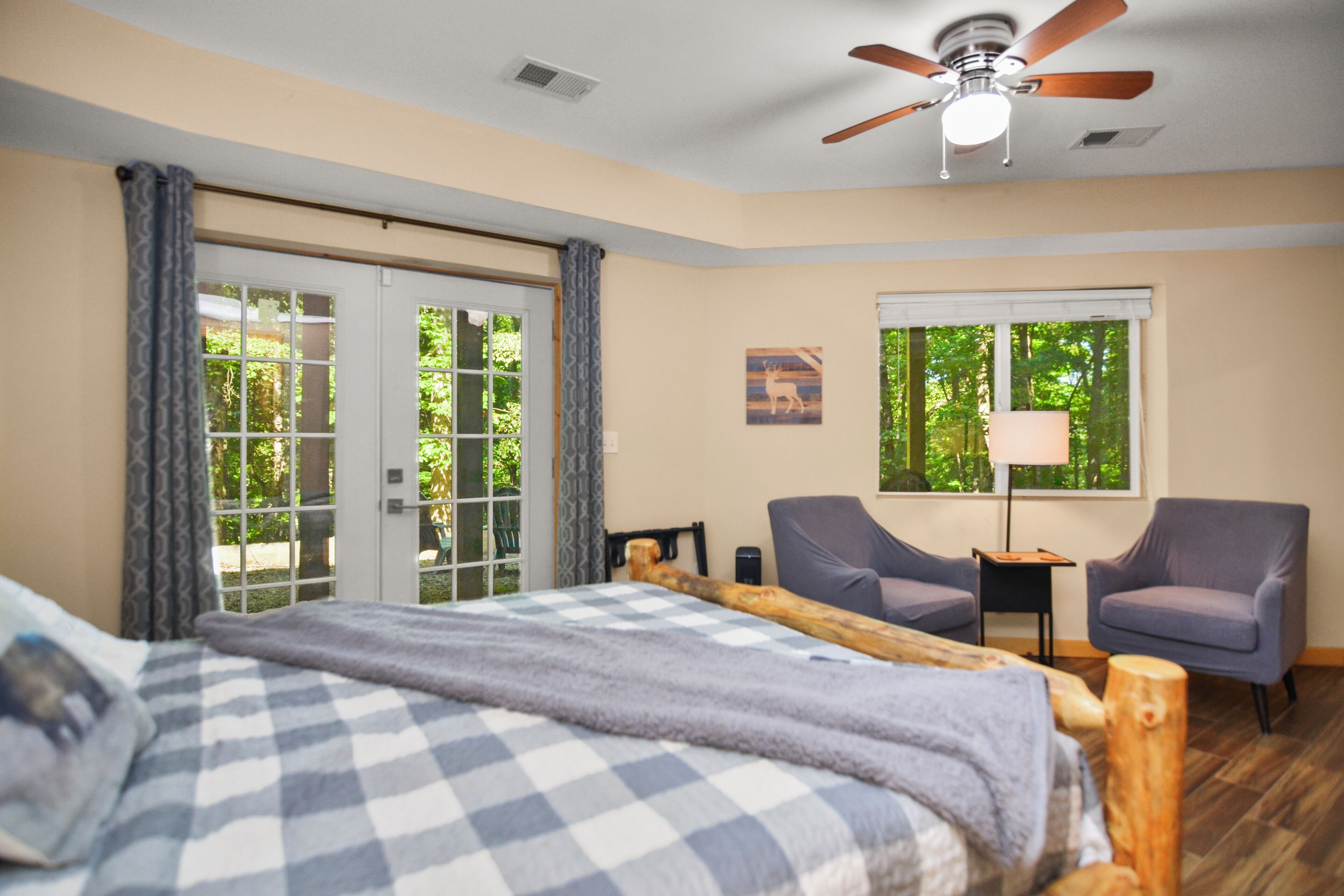 A bedroom with a bed, a ceiling fan, two chairs, a window with a view, and a door leading to an outdoor area.
