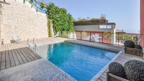A swimming pool with a wooden deck, a stone wall, and a building with a balcony. - Lovely apartment in La Turbie with house sea view (La Turbie)