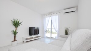 A modern living room with a flat-screen TV, a sofa, a potted plant, and a large window with sheer curtains. - Lovely apartment in La Turbie with house sea view (La Turbie)