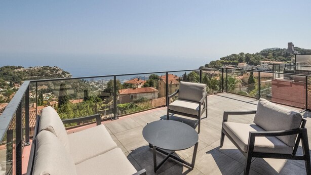 A balcony with two sofas and a round table, overlooking a coastal town with buildings and a hill. - Lovely apartment in La Turbie with house sea view (La Turbie)