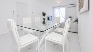 A modern, white-themed living room with a glass dining table surrounded by white chairs, a grey sofa, and a TV on a stand. - Lovely apartment in La Turbie with house sea view (La Turbie)