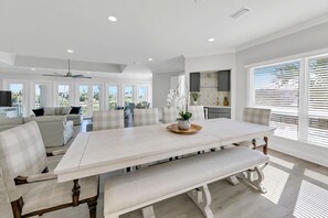 A spacious dining area with a large white table, cushioned chairs, and a bench.