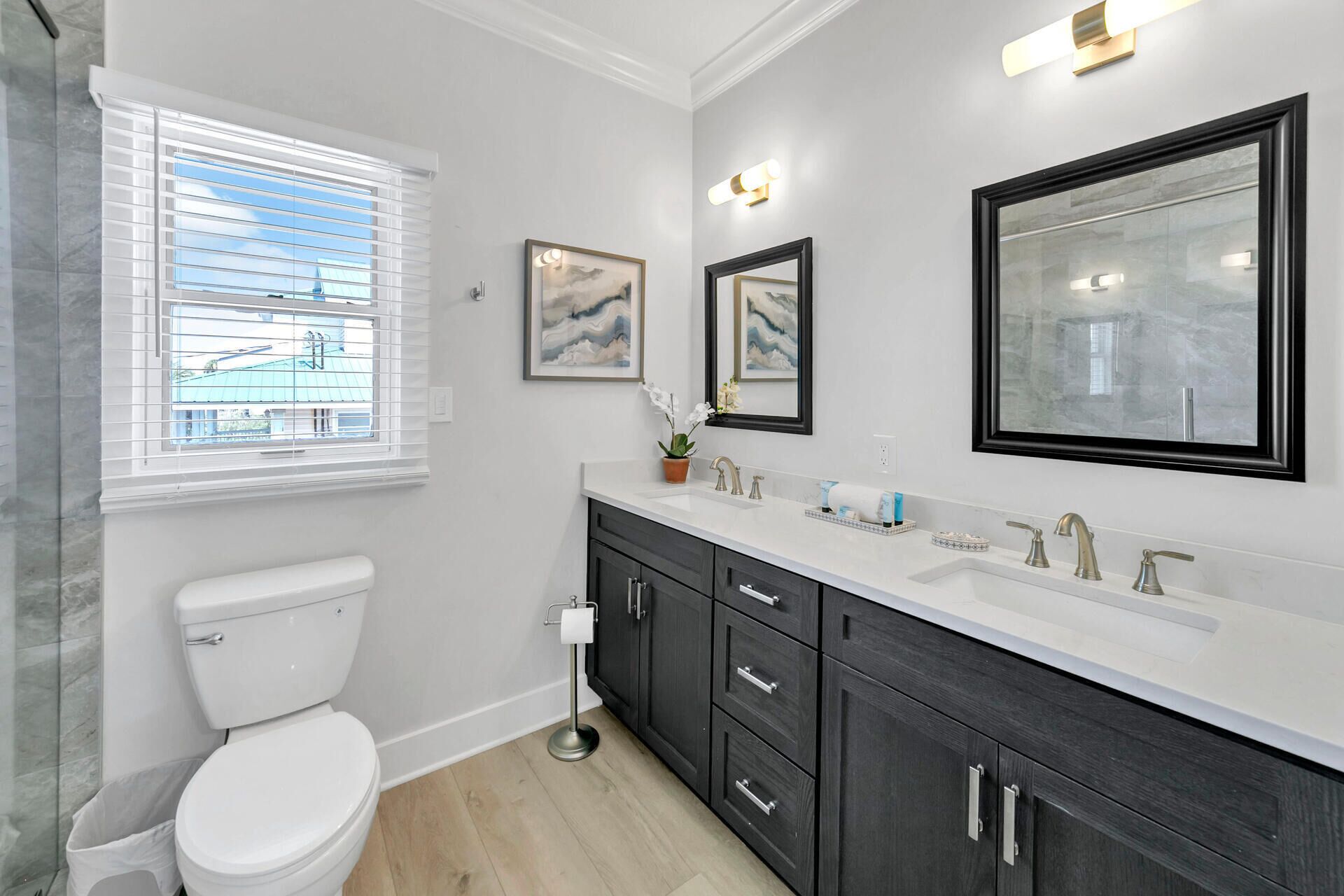 A modern bathroom with a toilet, dark wooden cabinets, a white sink, and framed artwork on the wall.