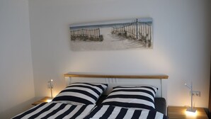 A bedroom with a bed, striped bedding, a headboard, bedside lamps, and a beach-themed wall art.