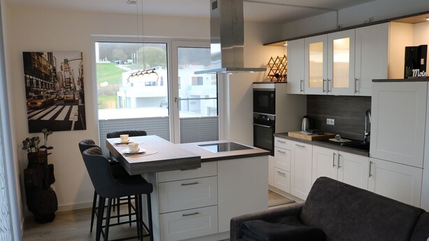 A modern kitchen with white cabinets, a built-in oven, and a large window overlooking a street.
