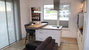 A modern kitchen with a central island, bar stools, a dining table, and a large window.
