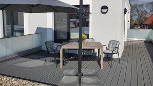 A modern outdoor patio with a table and chairs, a large umbrella, and a view of the surrounding area.