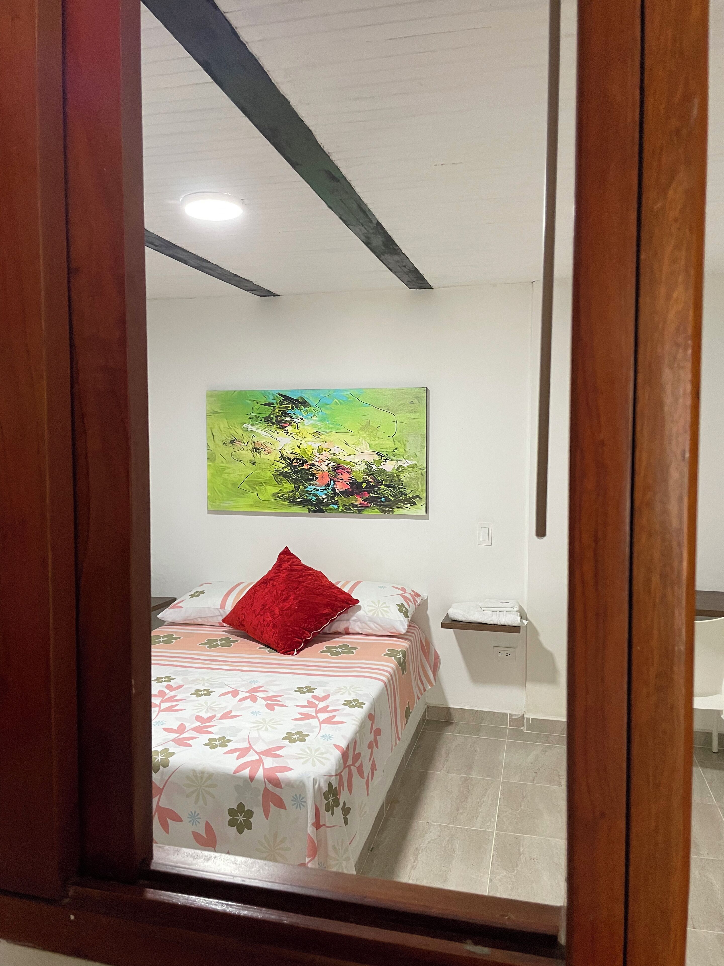 A bedroom with a bed, a nightstand, a painting on the wall, and a wooden door frame.