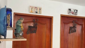 Twee houten deuren met metalen plaquettes, een blauwe vaas en een klein plankje met een beeldje en een plant.