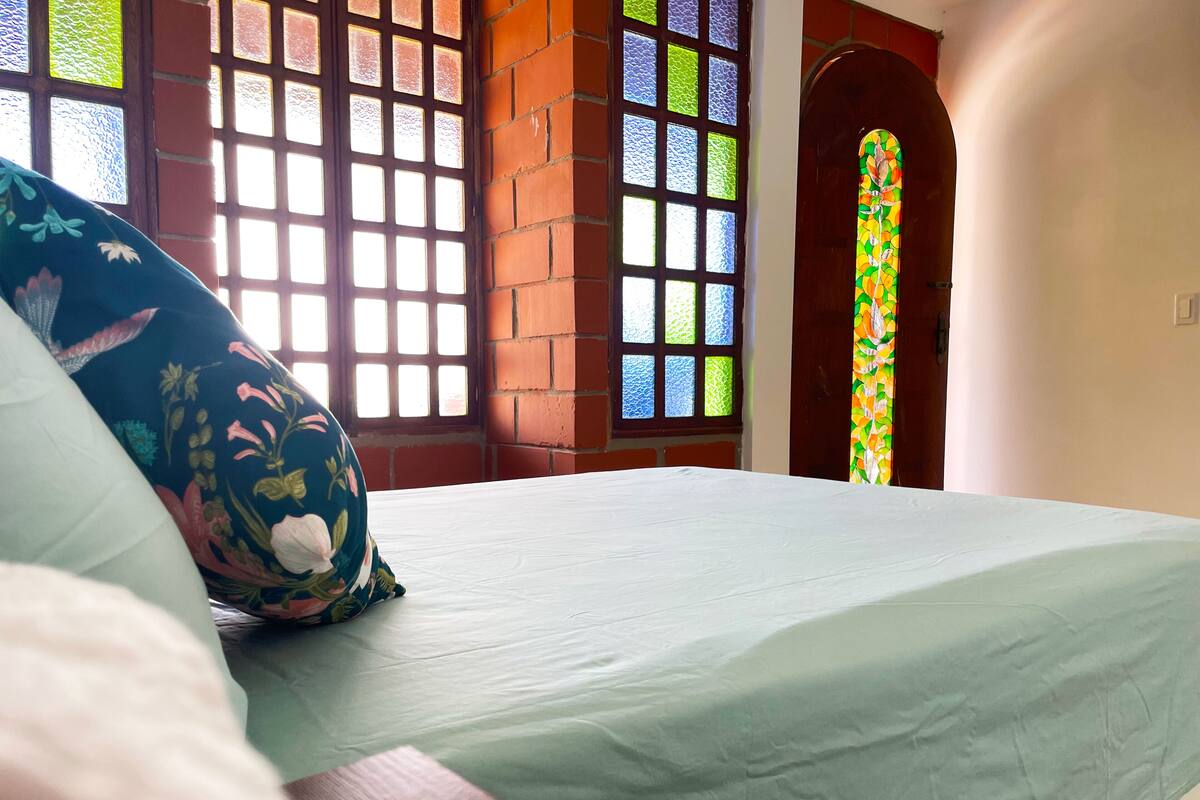 Un lit avec un coussin à motifs floraux, une couvre-lit verte et une fenêtre ornée de vitraux.