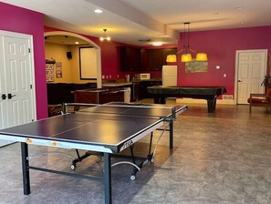 Uma sala de bilhar com mesa de sinuca, mesa de bilhar e mesa de tênis de mesa.