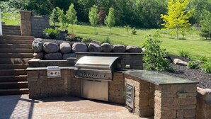 Une cuisine extérieure dotée d’un barbecue encastré, de murs en pierre et d’un plan de travail en pierre.