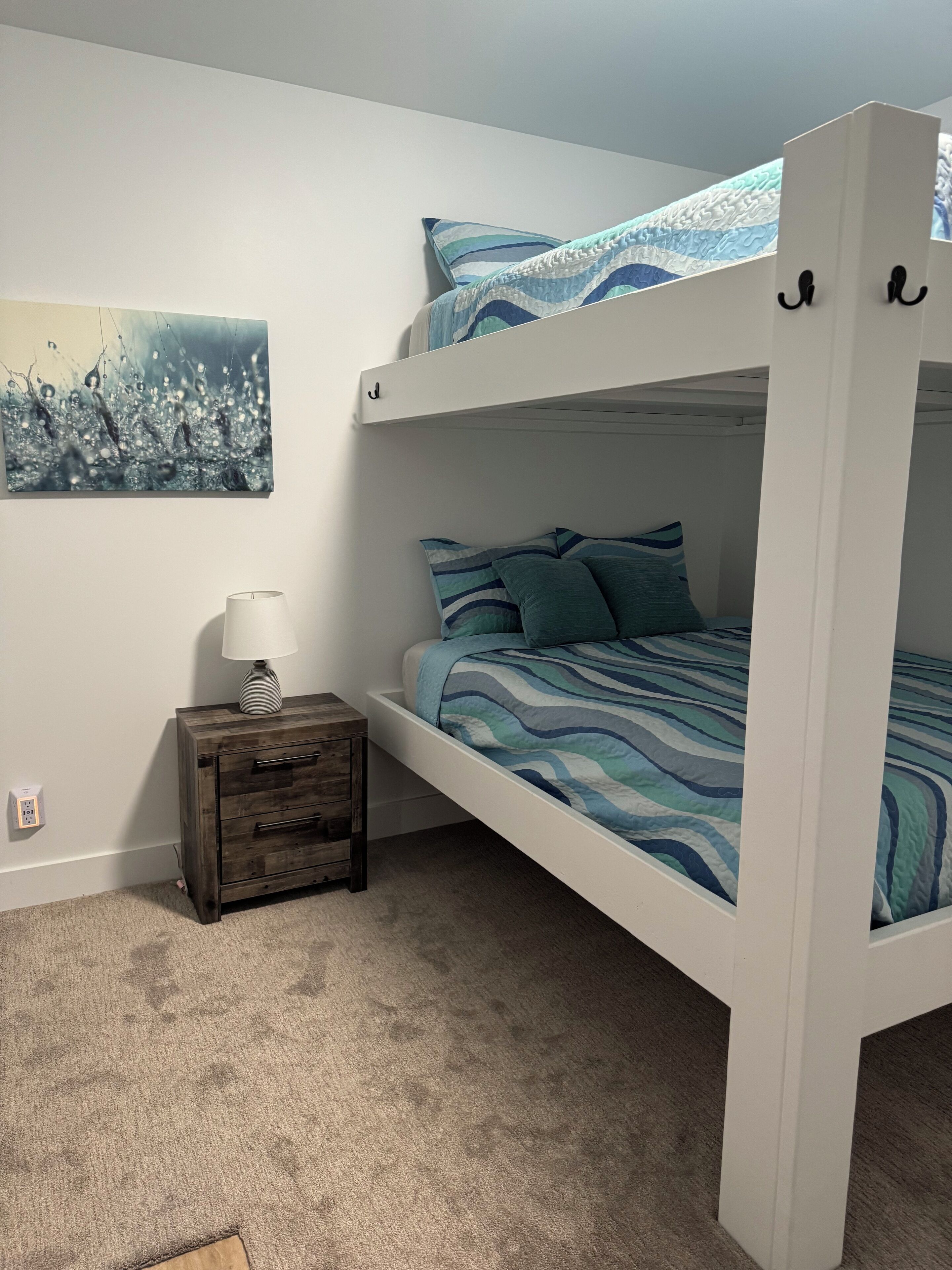 Un lit superposé avec une literie rayée bleue et blanche, une petite table de chevet en bois avec une lampe et un tableau accroché au mur.