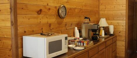 A wooden cabin kitchen with a microwave, coffee maker, and a clock on the wall.