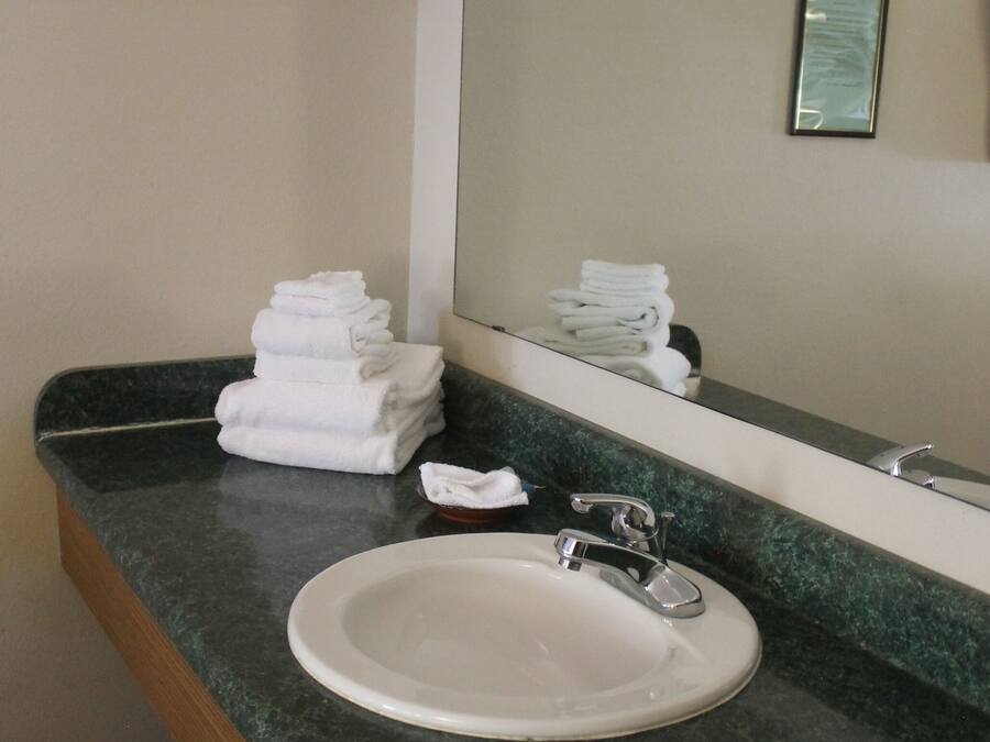 A bathroom with a sink, mirror, and stacked towels.