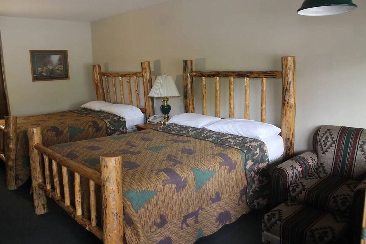 A room with two wooden beds, a patterned sofa, a lamp, and a framed picture on the wall.