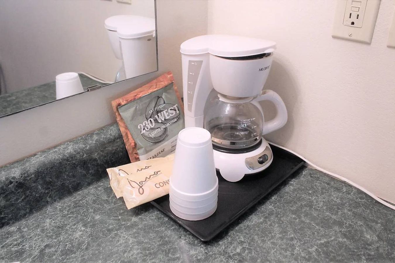 A coffee maker on a countertop with a framed coffee bag and disposable cups.