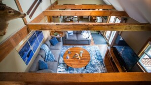 A loft-style living area with a wooden ceiling, gray sofas, a round coffee table, and a large window. - Trailside Lodge- Trail Access w/Game Table-New AC (Pittsburg)