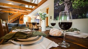 A dining table set with plates, glasses of red wine, a loaf of bread, and a vase with flowers. - Trailside Lodge- Trail Access w/Game Table-New AC (Pittsburg)