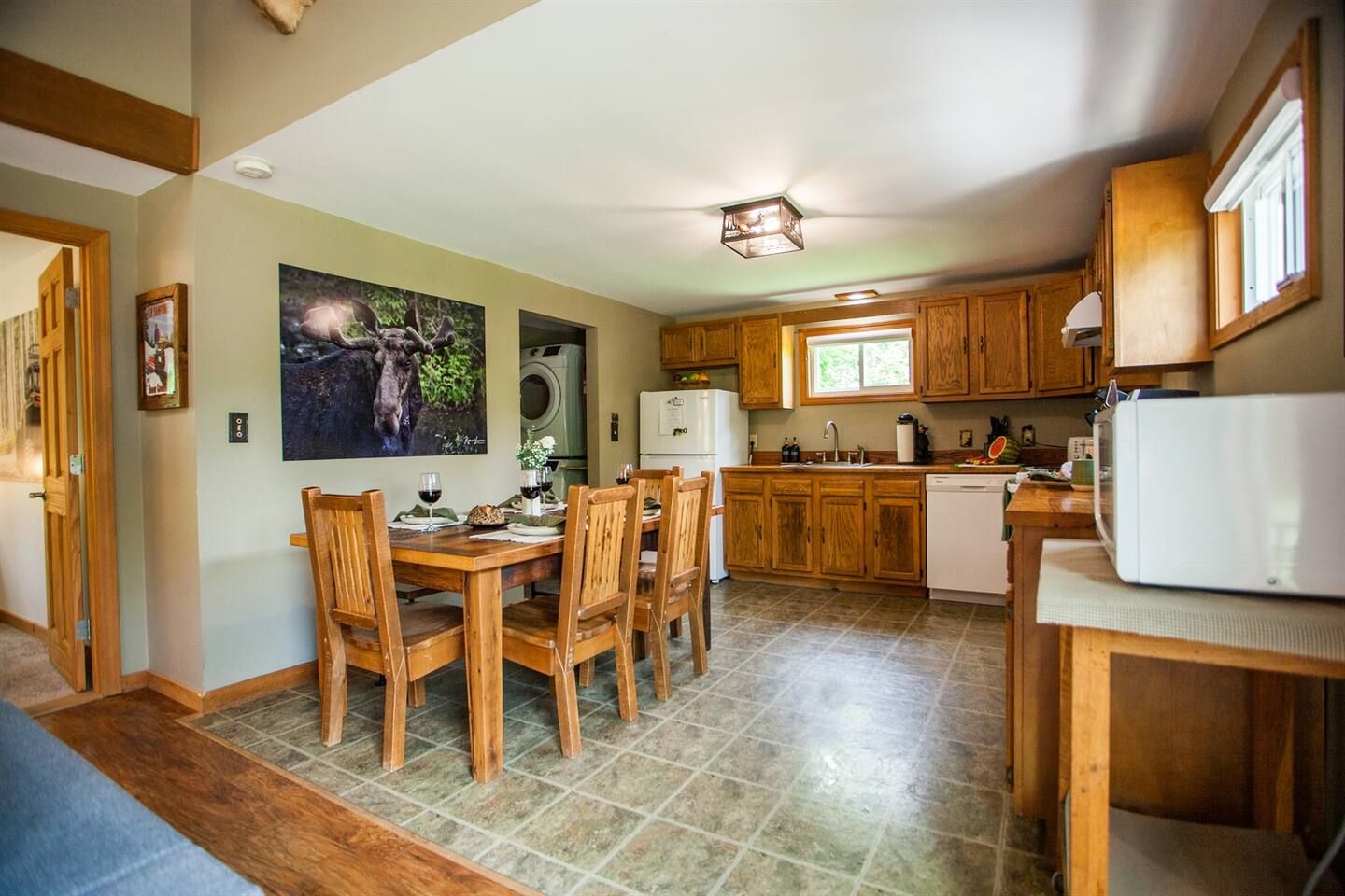 A compact kitchen with wooden cabinets, a dining table with chairs, a refrigerator, and a microwave.